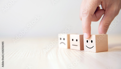 Close up customer hand choose smiley face and blurred sad face icon on wood cube, Service rating, satisfaction concept.