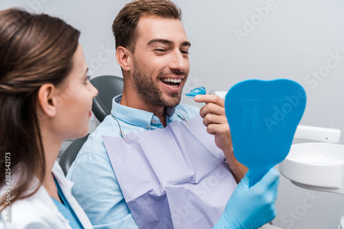selective focus of happy man looking at mirror and holding retainer near woman