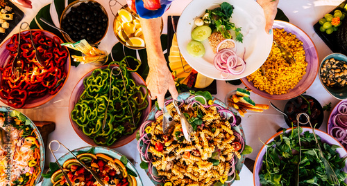 Vertical view of senior woman hand serving food on a dish from catering table during party celebration - catering and restaurant concept with mixed chef food on a table -coloured background 