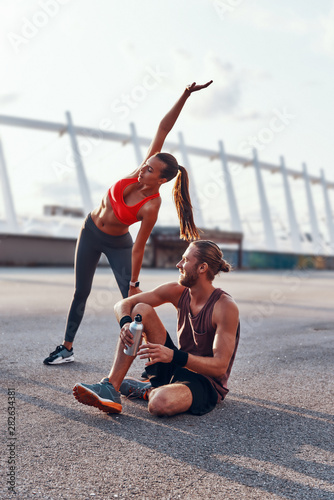 Young man and woman in sports clothing warming up and stretching outdoors