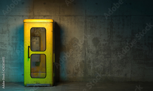 Single old yellow phone booth in retro style standing on the floor in front of the concrete wall at night time. Gloomy poorly lit interior in loft style with copy space. 3D rendering