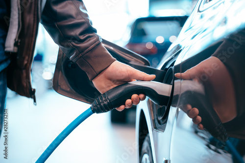 Human hand is holding Electric Car Charging connect to Electric car