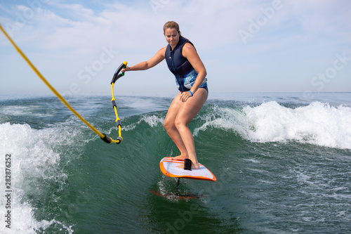A woman wake surfing and holding a tow rope.
