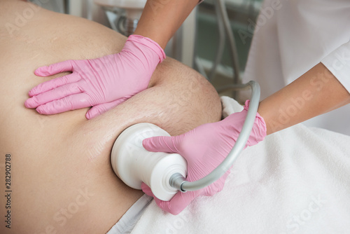 Closeup photo of fat man with big belly having cavitation procedure removing cellulite on abdomen in modern beauty clinic