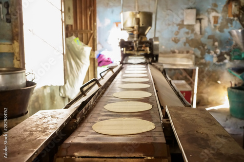 Las tortillas de maíz están saliendo en serie de la maquina antigua.