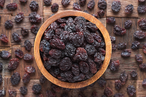 dried grapes, dark raisins in wooden bowl, top view.