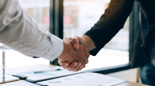 Entrepreneurs collaboration deal shaking hands in a modern office and financial paper graph on desk.