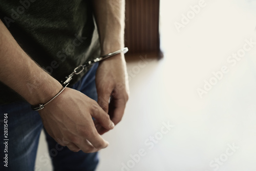 Man detained in handcuffs indoors, space for text. Criminal law