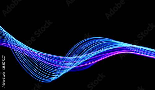 Long exposure, light painting photography. Vibrant streaks of neon blue and pink color against a black background.