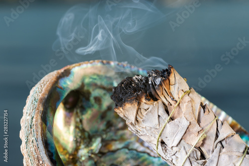 Smudging Ritual using burning thick leafy bundle of White Sage in bright polished Rainbow Abalone Shell on the beach at sunrise in front of the lake.
