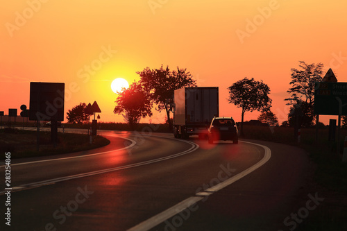 Samochód osobowy i ciężarowy, tir na tle zachodzącego słońca, droga ekspresowa.