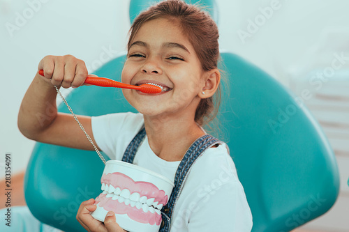 smiling mixed raced girl brushing teeth at dental clinic