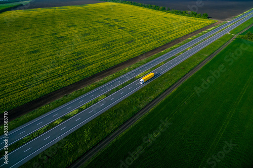 yellow truck driving on asphalt road along the green fields. seen from the air. Aerial view landscape. drone photography. cargo delivery Left side traffic
