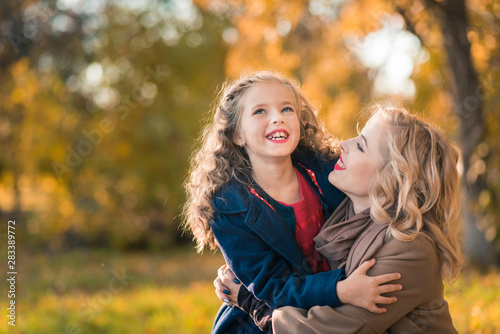 A portrait of a happy family: a young beautiful woman with her little cute daughter. Young daughter hugs mother in autumn colorful park outdoor. Mother's day