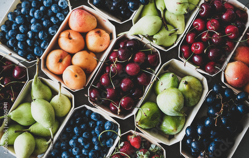 Summer fruit and berry variety. Flat-lay of ripe strawberries, cherries, grapes, blueberries, pears, apricots, figs in wooden eco-friendly boxes over grey background, top view. Local farmers produce