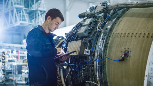 Aircraft Maintenance Mechanic Inspecting and Working on Airplane Jet Engine in Hangar