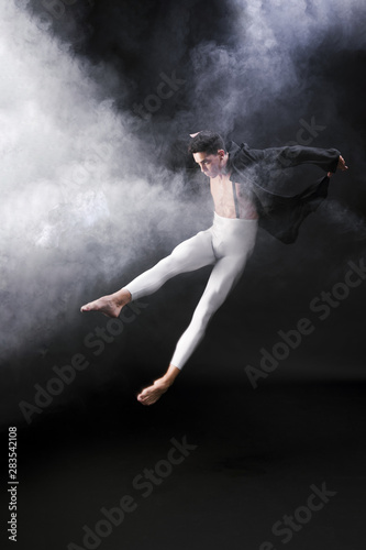 Young athletic man jumping and dancing near smoke against black background