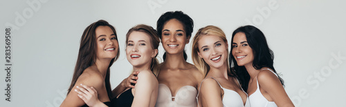 panoramic shot of five multiethnic girls smiling and looking at camera isolated on grey