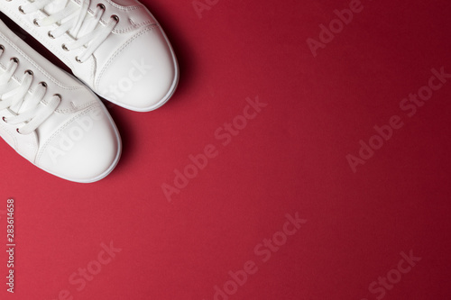 Pair of white trendy sneakers on red background. Place for text.