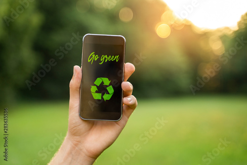 Go green concept, man in nature holding smartphone with go green text and recycle symbol 