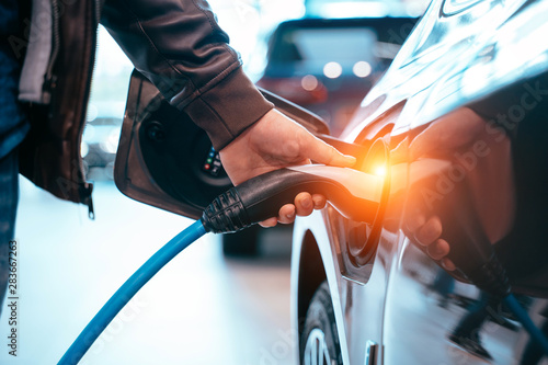 Human hand is holding Electric Car Charging connect to Electric car