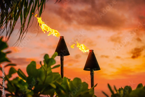 Hawaii luau party Maui fire tiki torches with open flames burning at sunset sky clouds at night. Hawaiian cultural travel vacation background.
