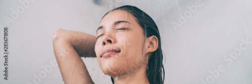 Shower woman taking hot bath rinsing hair in home bathroom. Asian girl under running water panorama banner header lifestyle.