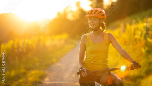 Pretty, young woman biking on a mountain bike enjoying healthy active lifestyle outdoors in summer (shallow DOF)