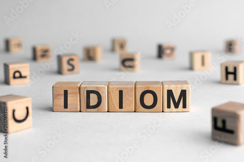 idiom - word from wooden blocks with letters, mode of expression concept, random letters around, white background