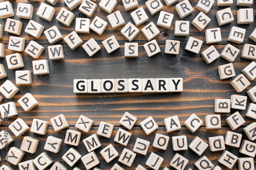 Glossary - word from wooden blocks with letters, alphabetical list with words meanings dictionary glossary concept, random letters around, top view on wooden background