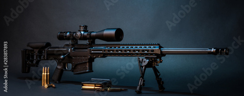 Modern powerful sniper rifle with a telescopic sight mounted on a bipod. Ammo and an additional magazine next to the rifle.