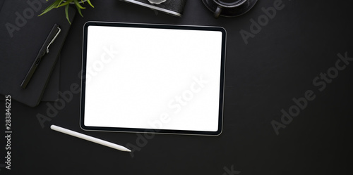 Blank screen tablet and office supplies in dark stylish workplace