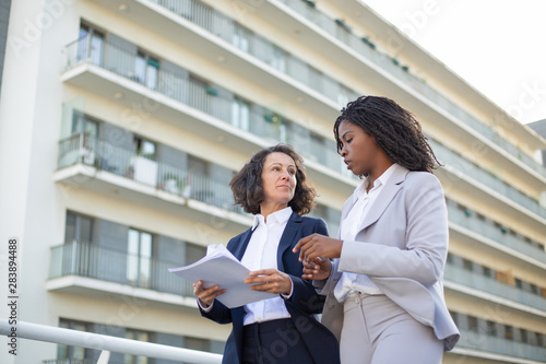 Multiethnic businesswomen discussing papers. Low angle view of professional female colleagues talking about documents on street. Business concept