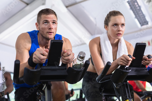 Male and female friend exercising on exercise bike in fitness center 