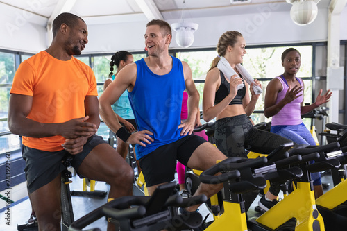 Fit people interacting with each other exercising on exercise bike in fitness center