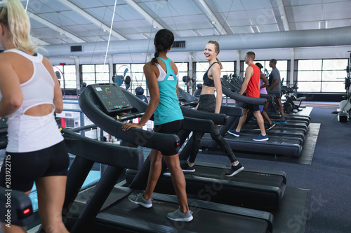Fit woman interacting with her female friend while exercising on treadmill