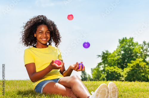 Girl juggle with balls on the lawn in park smiling