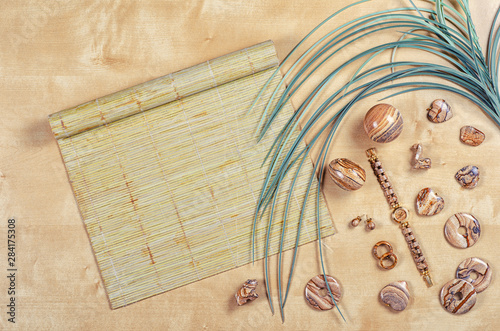 Flat lay different picture jasper items on wooden background with palm leaf and bamboo sushi rolling mat. Top view semi-precious stone jewelry concept.