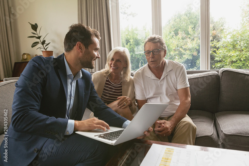 Active senior couple discussing with real estate agent over laptop in living room