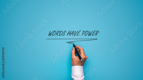 Male hand writing a Words have power sign with black marker on blue background.