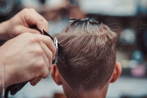 Boy getting haircut by barber in barbershop.