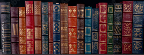 A stack of beautiful leather bound books with golden decoration against a black background.