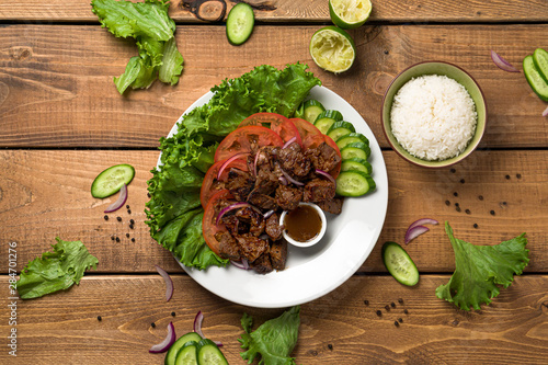  Bo Luc Lac flat lay from above view. Also named Lok Lak in cambodia or Shaking Beef in America. Tasty marinated sauteed beef cubes are served with fresh lettuce, tomatoes, cucumbers, onions and rice.