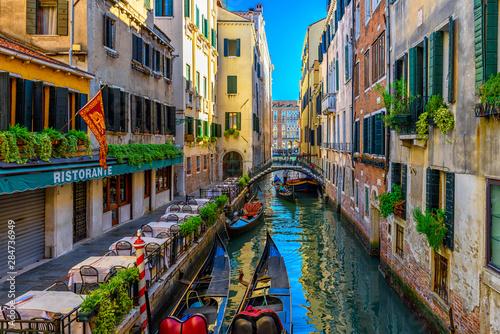 Narrow canal with gondola and tables of restaurant in Venice, Italy. Architecture and landmark of Venice. Cozy cityscape of Venice.