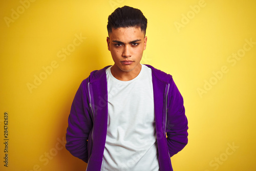 Young brazilian man wearing purple sweatshirt standing over isolated yellow background skeptic and nervous, frowning upset because of problem. Negative person.