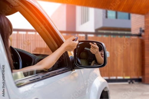 Woman in car, hand using remote control to open auto wooden door with modern home blurred background. Automatic gate concept