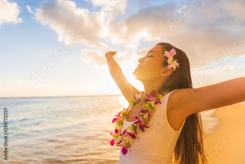 Hawaii hula luau woman wearing hawaiian lei flower necklace on Waikiki beach dancing with open arms free on hawaiian vacation. Asian girl with fresh flowers hair, traditional polynesian dance.