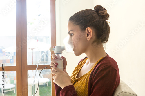 Young woman doing inhalation nebulizer in hospital, holding a mask nebuliser inhaling asthma and bronchitis medication to improve breathing. Healthcare, medicine, disease concept.