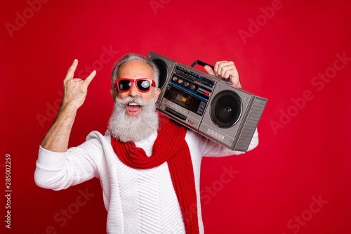 Rock chritmastime Portrait of crazy santa in eyeglasses eyewear screaming showing swag sign holding boom box wearing white sweater isolated over red background