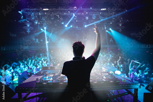 Silhouette of DJ in nightclub with hands up, shot from behind